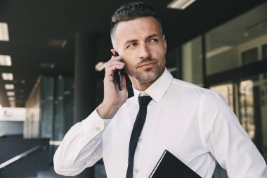 Kendine güvenen genç işadamı portresi ile ağıl cam bina dışında duran ve cep telefonu üzerinde konuşurken resmi elbise giymiş