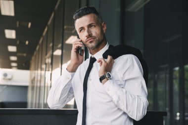 Resmi elbise ceket omzunun üzerine bina ve cep telefonu üzerinde konuşurken bir cam dışarıda yakışıklı bir genç işadamı portresi giymiş