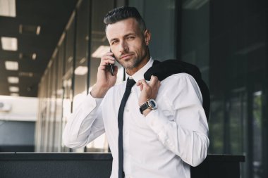 Resmi elbise ceket omzunun üzerine bina ve cep telefonu üzerinde konuşurken bir cam dışarıda başarılı bir genç iş adamı portresi giymiş