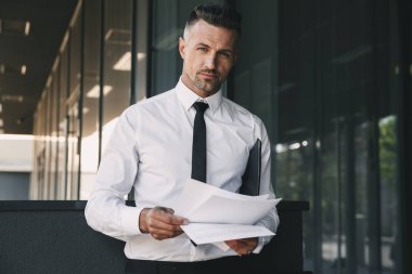 Başarılı bir genç iş adamı portresi cam binanın önünde duran ve belgeleri seyir resmi elbise giymiş