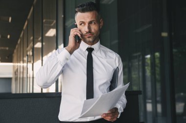 Kendine güvenen genç işadamı portresi cam binanın önünde duran ve cep telefonu üzerinde konuşurken resmi elbise giymiş