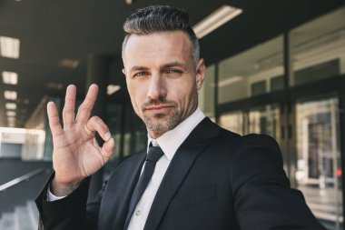 Başarılı bir genç iş adamı portresi cam binanın önünde duran ve bir selfie alarak takım elbise giymiş