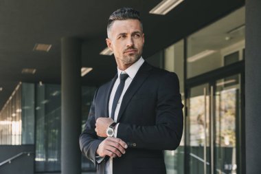 Yakışıklı bir genç işadamı portresi cam binanın önünde duran ve onun kol dokunmadan takım elbise giymiş