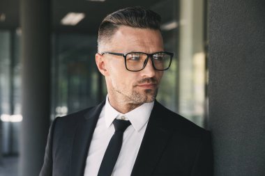 Takım elbise duran cam bina dışında kendine güvenen genç işadamı portresi giymiş