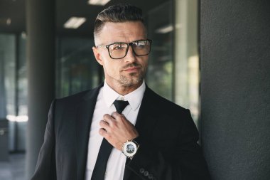 Kendine güvenen genç işadamı portresi cam binanın önünde duran ve kravatını dokunmadan takım elbise giymiş