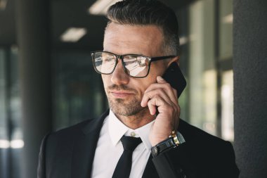 Yakışıklı bir genç işadamı portresi cam binanın önünde duran ve cep telefonu üzerinde konuşurken takım elbise giymiş