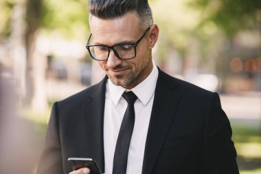 Dışında yürüme ve cep telefonuyla takım elbise giymiş bir gülümseyen işadamı portresi