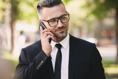 Mutlu bir işadamı portresi dışında yürüyüş ve cep telefonuyla takım elbise giymiş