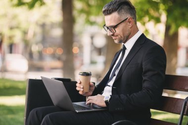 Başarılı bir iş adamı portresi dışında dizüstü bilgisayar ile bir bankta oturan ve kahve içme resmi kıyafet giymiş