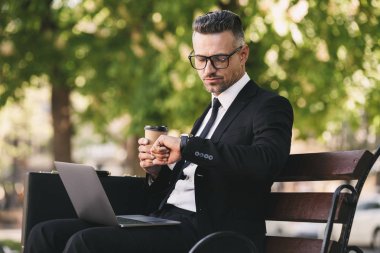 Başarılı bir iş adamı portresi dışında dizüstü bilgisayar ile bir bankta oturan ve kahve içme resmi kıyafet giymiş