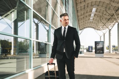 Kendine güvenen işadamı ile bir bavul Havaalanı terminal dışında yürüme takım elbise giymiş