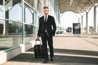 Yakışıklı işadamı ile bir bavul Havaalanı terminal dışında yürüme takım elbise giymiş