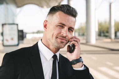 Yakışıklı işadamı Havaalanı terminal dışında yürüyüş ve cep telefonu üzerinde konuşurken takım elbise giymiş
