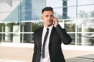 Gülümseyen iş adamı Havaalanı terminal dışında yürüyüş ve cep telefonu üzerinde konuşurken takım elbise giymiş