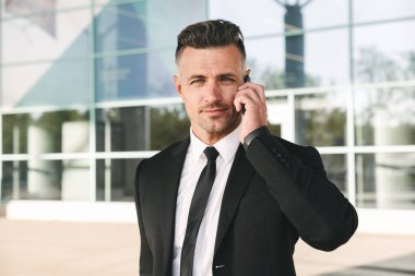 Gülümseyen iş adamı Havaalanı terminal dışında yürüyüş ve cep telefonu üzerinde konuşurken takım elbise giymiş