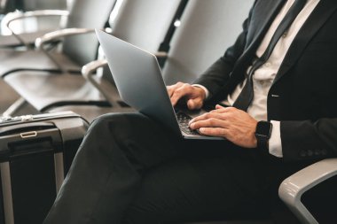 Havaalanı lobisinde otururken dizüstü bilgisayar kullanan takım elbise giymiş işadamı yakın çekim
