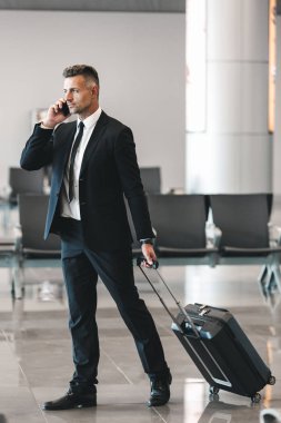 Bavulla Havaalanı Lobide yürürken cep telefonu üzerinde konuşurken kendinden emin olgun işadamı