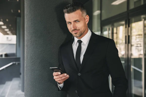 Portrait Smiling Young Businessman Dressed Suit Standing Glass Building Using — Stock Photo, Image