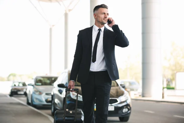 Уверенный Зрелый Бизнесмен Разговаривает Мобильному Телефону Выходя Аэропорта Чемоданом — стоковое фото
