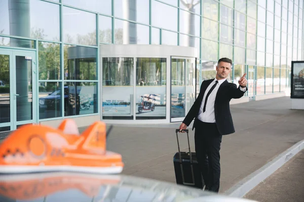 严肃的商人走在机场外面与手提箱和捉住出租汽车 — 图库照片
