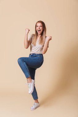 Tam uzunlukta başarı ile açık ağız bej renkli arka plan üzerinde izole kutlama heyecanlı bir casual kız portresi