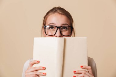 Kitap yüzüne tutarak ve bej renkli arka plan üzerinde izole ararken Eyewear bir genç kız portresi