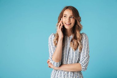 Gülümseyen smartphone ile konuşmak ve uzak mavi arka plan üzerinde seyir elbiseli sarışın kadın