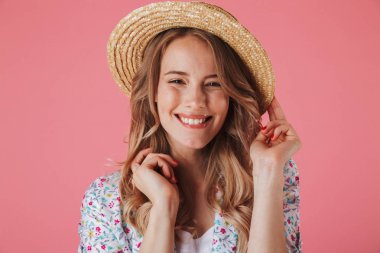 Yazlık elbise ve hasır şapka pembe arka plan üzerinde izole kamera bakarak memnun genç bir kadın portresi kapatın