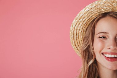 Hasır şapka pembe arka plan üzerinde izole kopya alanı ile kameraya bakarak mutlu genç bir kadın portresi yarım yüz kadar kapatın