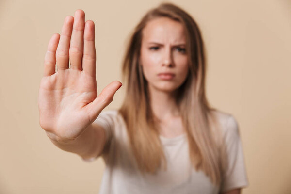 Portrait of a serious young woman showing stop gesture with her palm isolated over beige background