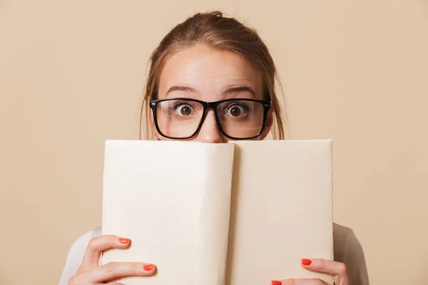 一个年轻的女孩在眼镜持有书在她的脸上孤立的米色背景的肖像 — 图库照片