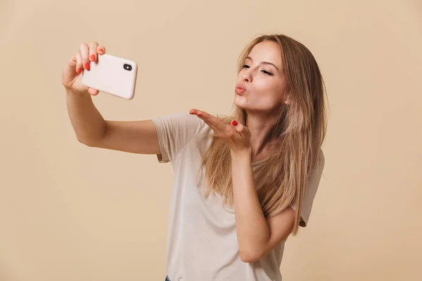 Portrait Happy Young Girl Taking Selfie Blowing Kiss Isolated Beige — Stock Photo, Image