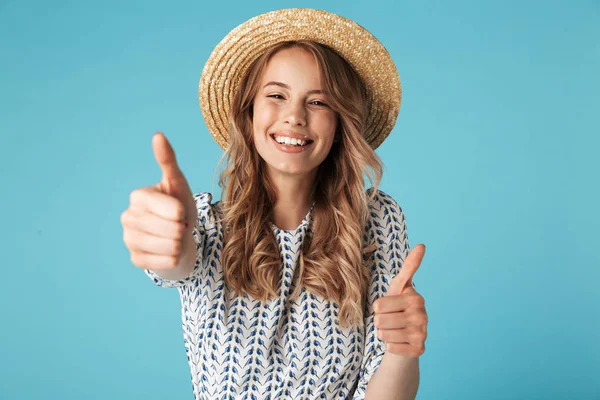 快乐的金发女人在礼服和帽子显示竖起大拇指 看着在蓝色背景的相机 — 图库照片