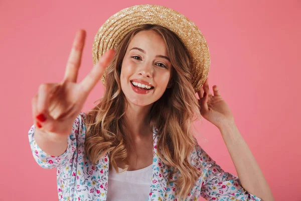 关闭在夏季礼服和草帽显示和平姿态隔离粉红色背景的年轻女子的肖像 — 图库照片