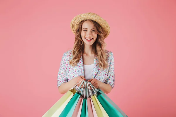 一个年轻快乐的女人在夏天的礼服和草帽持有购物袋 在粉红色背景隔离 — 图库照片