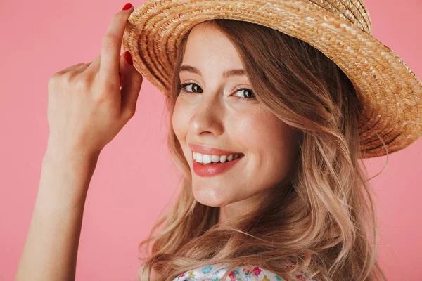 关闭在夏季礼服和草帽摆出一个迷人的年轻女子的肖像和看着在粉红色背景隔离相机 — 图库照片