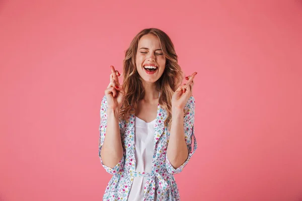 一个兴奋的年轻女子的肖像在夏季礼服持有手指交叉为好运孤立的粉红色背景 — 图库照片