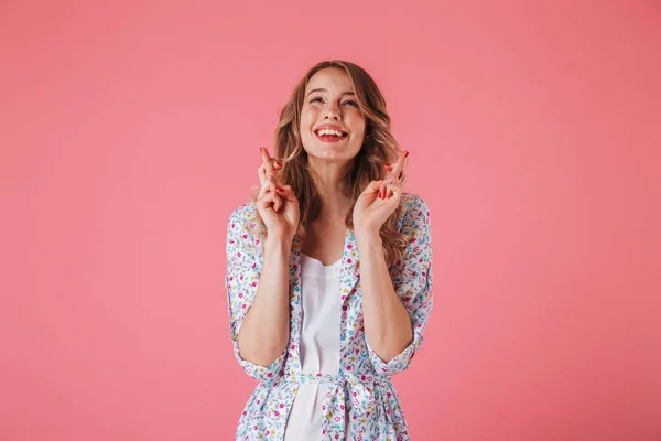 夏のドレスとピンク背景に分離見上げると幸運のための交差の指を保持して興奮した若い女性の肖像画 — ストック写真
