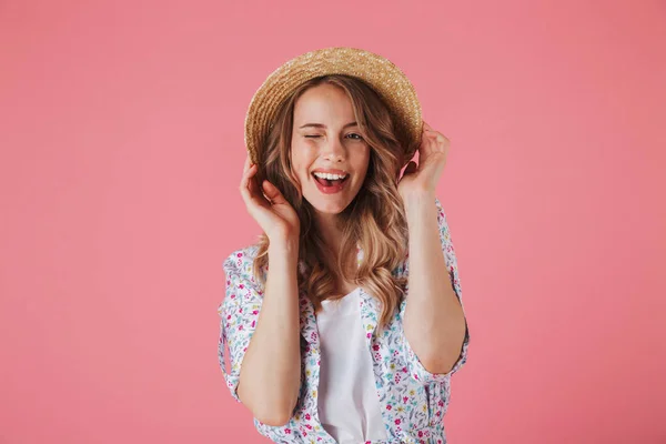 一个微笑的年轻女子的肖像在夏季礼服看着相机和眨眼的粉红色背景 — 图库照片