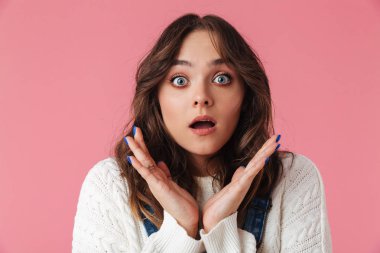 Poz ve kameraya pembe arka plan üzerinde seyir rahat kıyafetler sürpriz esmer kadın