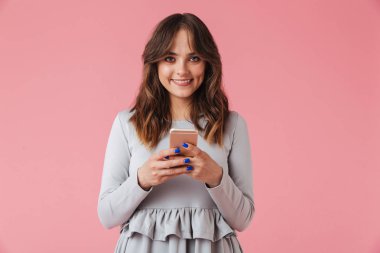 Görüntü izole istimal hareket eden telefon fotoğraf makinesi görünümlü pembe duvar arka plan üzerinde duran sevimli genç güzel kadın.