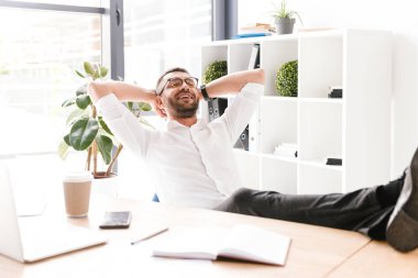 Mutlu adam beyaz gömlek ve office ayaklı masada oturan ve başının arkasında elele gözlük görüntüsünü