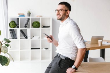 İcra Müdürü adam ofiste tabloda oturan ve cep telefonu kullanırken büyük pencereden bakarak formal giyim görüntü