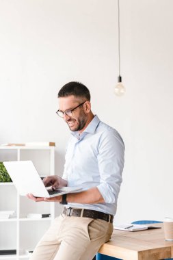 Ofiste tabloda oturma ve iş sohbet gümüş dizüstü bilgisayarda sahip beyaz gömlek giymiş yakışıklı neşeli adam