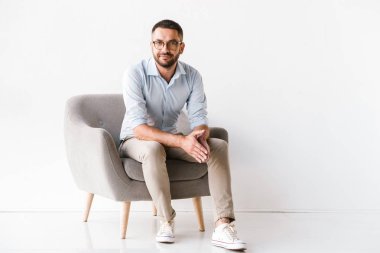 Yatay koltukta oturan ve beyaz arka plan üzerinde izole kamera bakarak şık resmi elbiseler giyen çekici beyaz adam portresi