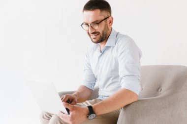 Yatay koltukta oturan ve beyaz arka plan üzerinde izole dizüstü bilgisayar üzerinde çalışan şık resmi elbiseler giyen sakallı beyaz adam portresi