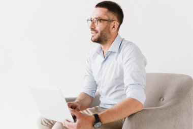 Yatay koltukta oturan ve beyaz arka plan üzerinde izole dizüstü bilgisayar üzerinde çalışan şık resmi elbiseler giyen sakallı beyaz adam fotoğrafı