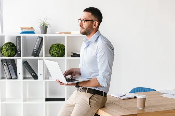 在办公室桌子上穿着白衬衫的务实男士形象图象 用银膝上型电脑工作时向前看 — 图库照片