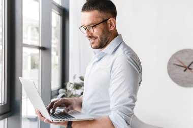 İş iç çalışması sırasında gümüş dizüstü tutarak başarı ifade beyaz gömlek giymiş memnun office adam görüntüsünü