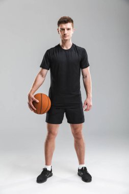 Yakışıklı bir genç sporcu gri arka plan üzerinde izole bir basketbol ile ayakta tam uzunlukta portresi